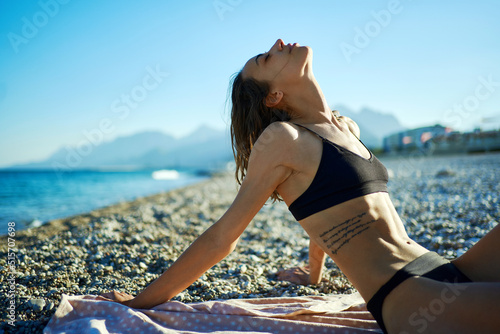Beautiful sensual woman in black bikini sunbathing at sea beach next to mountains during vacation