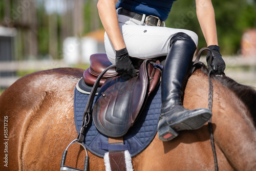 A rider sits on her horse and adjusts her stirrup leather.
