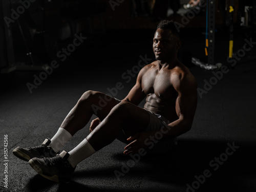 Afro american man doing abdominal exercises in a dark studio. 