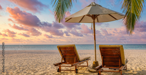Beautiful tropical sunset landscape two lounge chairs, beds, umbrella under palm tree leaves. White sand sea view with horizon, colorful twilight sky, calmness and relaxation. Luxury beach destination