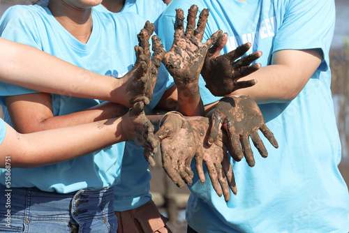 Group of four volunteer in blue t-shirt showing join hands covered mud dirty after planting sapling tree in deep mud at mangrove forest, do charity work together, love our planet earth for further