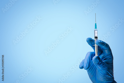 Doctors hand in surgical gloves holds a syringe on classic symbolic blue background