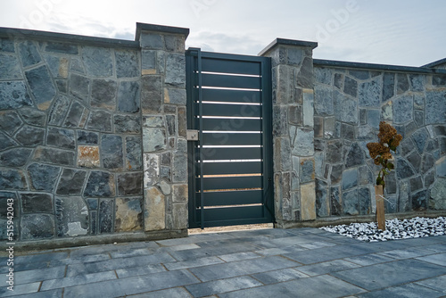 Stone high fence with shut iron door in paved yard of modern style design property outdoor