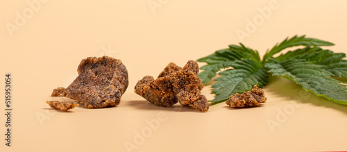 brown pieces of hashish and green cannabis leaf on a yellow background.