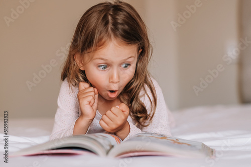 Emotional child girl read interesting book in bed. Small kid enjoy reading. Fantasy and fantastic. Developing child fantasy and imagination. Imaginary world. Fairy tale. Bedtime reading