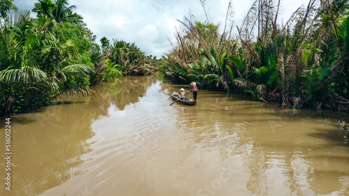 tourist on sampan boat cruise in the Mekong river canals with woman paddling in Vietnamese hat