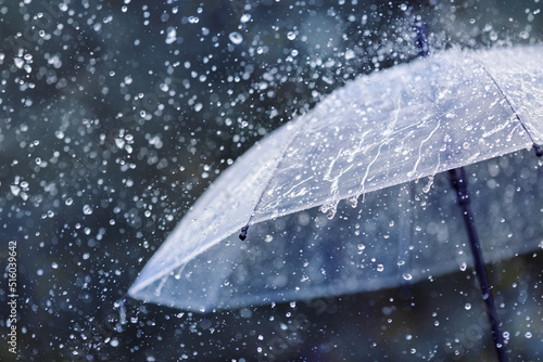 Transparent umbrella under heavy rain against water drops splash background. Rainy weather concept.