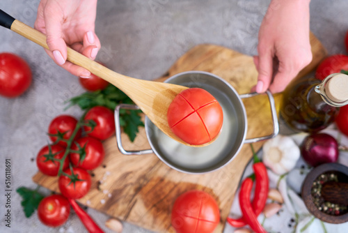 woman blanching a tomato holding over pan with hot water for further peeling