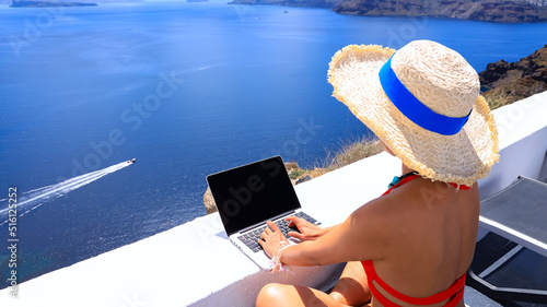 Back view of digital nomad woman freelancer as running remotely with bright scenic view of the Mediterranean Sea ,Oia -Santorini,Greece