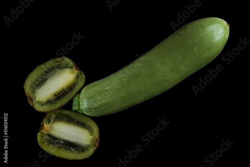 2 two halves of Kiwi fruits with seeds and zucchini in the shape of a penis isolated on black background.