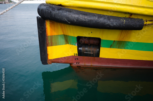 Bow of yellow boat with waterline, fairlead, raised anchor, rubber fender and draft marks on ship bow. Ship bow of fishing boat close-up. Front part of hull of fishing vessel with traces of rust