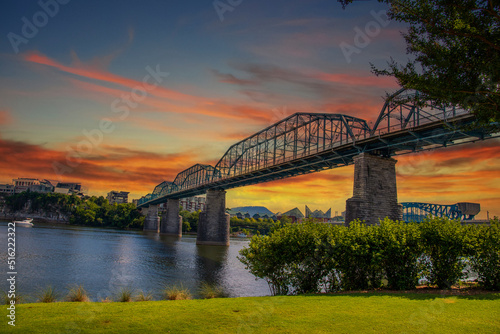 the majestic Walnut Street Bridge over the rippling blue waters of the Tennessee River surrounded by lush green trees and buildings with powerful clouds at sunset at Coolidge park in Chattanooga