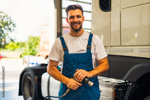 Mechanic is standing in his workshop and holding tools. He is ready to repair trucks, cars, and buses. Worker in the auto-mechanic workshop