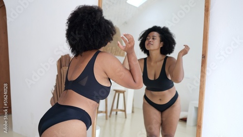 Multicultural plus size woman in lingerie looking at her body in the mirror. Black woman struggles with obesity and overweight, wants to lose weight and be slim Woman body positive without criticism