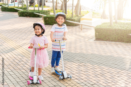 Child riding scooter. Happy Asian little kid boy and girl wear safe helmet play kick board on road in park outdoors on summer day, Active children games outside, Kids sport healthy lifestyle concept