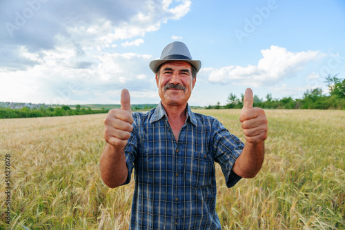 Elderly farmer man with mustache shows thumb up, looking at camera.