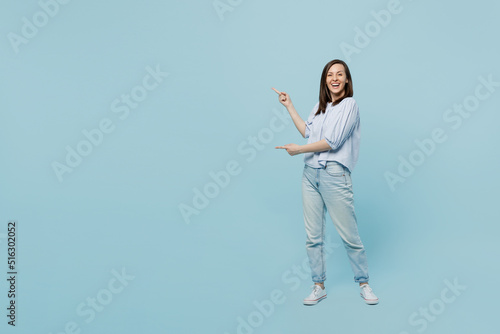 Full body young happy fun woman she 20s wears casual blouse indicate point index finger aside on workspace area mock up isolated on pastel plain light blue background studio. People lifestyle concept.