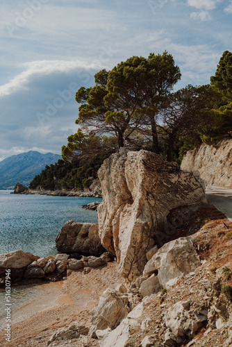 Beautiful view of a beach in Croatia with big rocks, pebbly beach, pine trees and high mountains over the coastline.