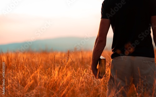 Human praying on the holy bible in a field during beautiful sunset.