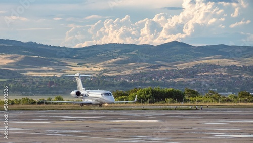 White business jet with turbofan engines on the airport with attractive panoramic mountain landscape and cloudy sky. Modern technology in fast transportation, business travel and tourism, aviation.