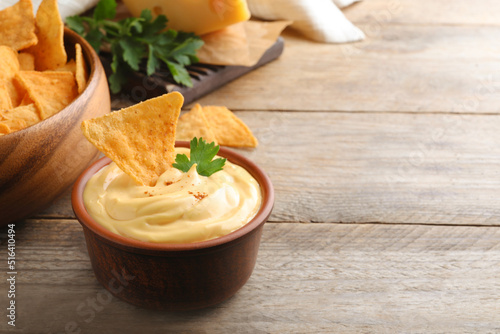 Delicious cheese sauce with nacho and parsley on wooden table, space for text