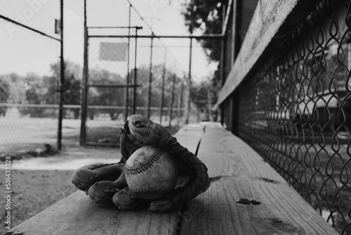 Old used baseball equipment on field dugout bench in black and white closeup.