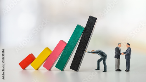 Overcoming fear of failure, domino effect or chain reaction, psychology concept : Businessman CEO as an action taker pushes and prevents wood bar graph from collapsing, two dearlers negotiate a deal.