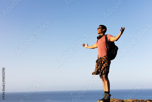 Young man standing on the stone with raised up arms. Tourist man on the top of the mountain...