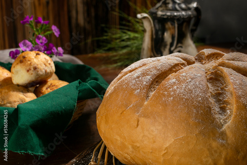 Natural homemade round country bread with smaller loaves with an old teapot decorated with ears of wheat on a country table