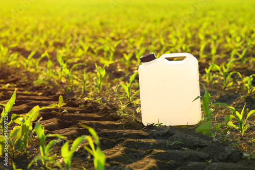 Blank white herbicide canister can in corn seedling field in springtime sunset