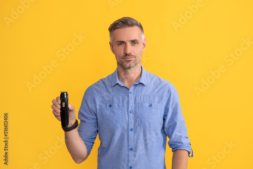 man hold electric razor on yellow background, shaving
