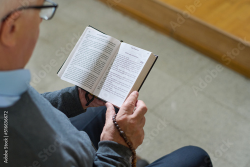 Above shot of mature man in casualwear holding open Holy Bible while reading one of Gospels during sermon in church