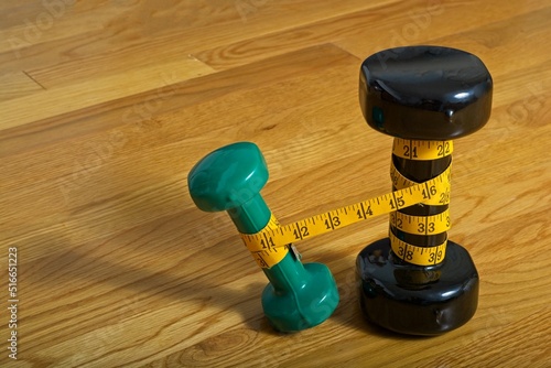 Two standing dumbbells, wrapped in measuring tape with light weight leaning away