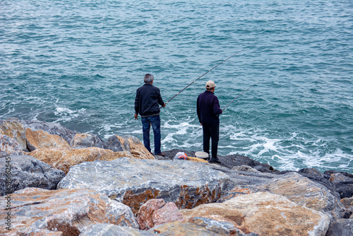 Fishermen are fishing while sitting on the stones on the sea promenade on a cloudy day