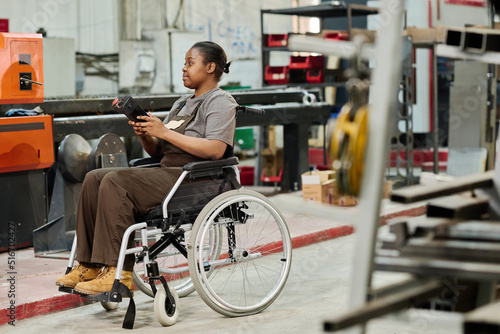 African worker with disability sitting in wheelchair and working at machine with remote control