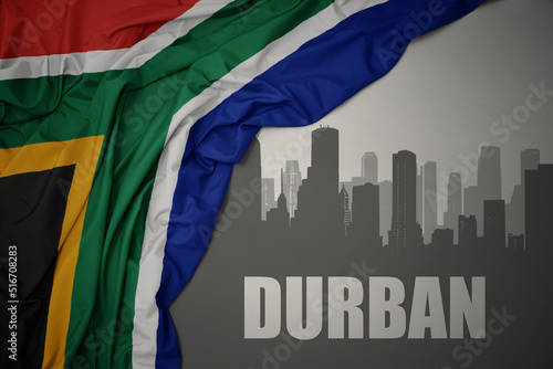 abstract silhouette of the city with text Durban near waving colorful national flag of south africa on a gray background.