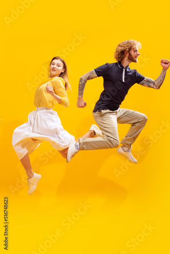 Portrait of young man and woman in casual clothes posing isolated over yellow studio background. Jumping in excitement