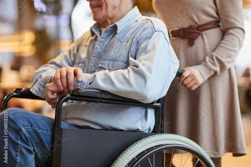 Close-up of female volunteer in dress pushing aged man in wheelchair while working with handicapped man in nursing home