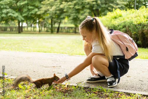 happy schoolgirl in uniform with backpack feeds a squirrel in the park on her way to school