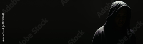 Silhouette of hooligan in hoodie with lighting isolated on black, banner