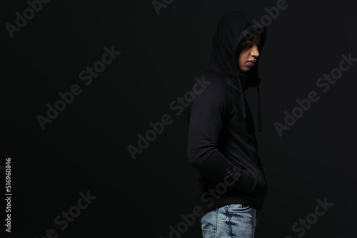 Side view of african american hooligan in hoodie standing isolated on black