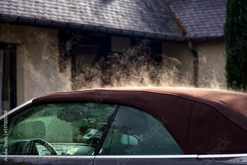 Closeup of car with evaporating steam on roof the background of house under morning rays of the sun