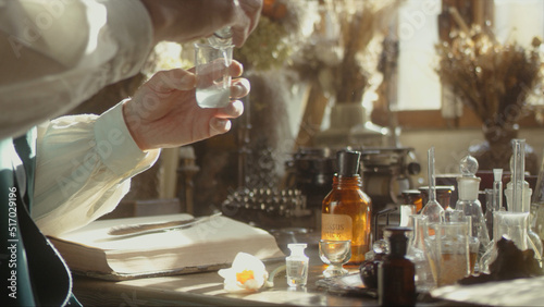 A close-up of a perfumer at his desk looking for a new fragrance. Vintage cinematic concept. Sunny day in the workshop. Lots of ingredients, glass flasks on the table. Concept of perfumery