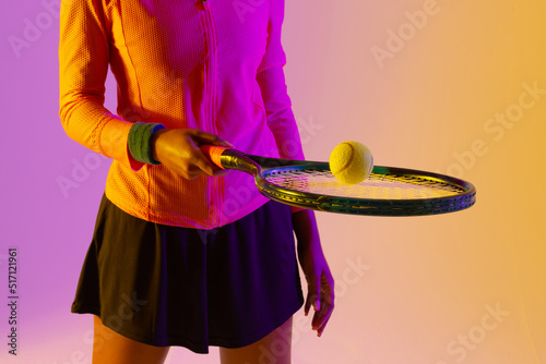 Image of midsection of african american female tennis player in neon violet and yellow lighting