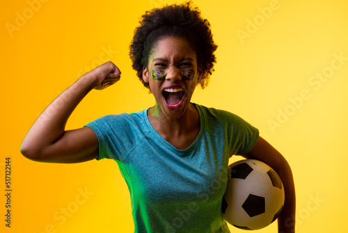 Image of african american female soccer fan with flag of portugal cheering in yellow lighting