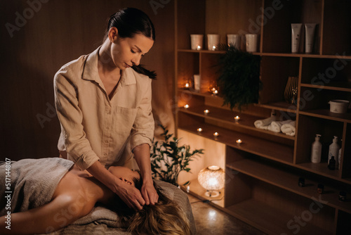 A masseuse gives a body massage to a woman in a spa center. A professional masseur massages the shoulder of a girl lying in a spa center