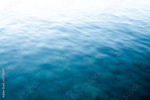 Blue water surface. Turquoise sea waves. Transparent sea water with rocks on bottom. Defocused image for background. Waves texture. Blurred image