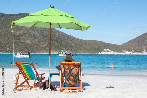 Man with sun hat on colorful sun loungers next to umbrella, on the paradisiacal beaches of Pontal do Atalaia Cabo Frio, Brazil. 