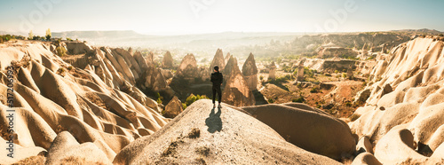 Thoughtful Female person stand look over dramatic valley on hazy morning sunrise with fairy chimneys background. Solo exploration in Turkey. Cinematic Travel destination-Cappadocia