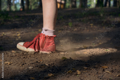 A man in red sneakers runs on the ground in a forest park. Forest, a place to relax and play sports. From under the sole flies dust and dirt close-up. Typing soft focus